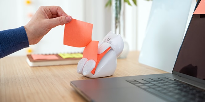 Una persona che prende un Foglietto Post-it® da un distributore di Foglietti Post-it® bianco a forma di gufo
