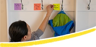 Una mamma che posiziona dei foglietti Post-it® colorati con messaggi positivi e li attacca accanto agli appendiabiti nel corridoio
